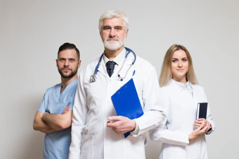 Na zdjęciu trzech specjalistów ochrony wzroku: okulista, optometrysta i ortoptysta stoją razem w białych fartuchach, symbolizując kompleksową opiekę nad pacjentem. Fotografia ilustruje artykuł o współpracy okulista optometrysta ortoptysta, pokazując zespół ekspertów dbających o zdrowie i komfort widzenia.